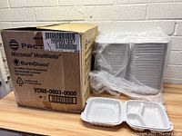 Stacks of white 8" x 8" food containers wrapped in plastic next to the box. Two containers shown open displaying three compartments (one larger and two smaller).