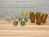 Full view of assorted glassware set showing all types together on a wooden surface against a light grey brick wall.
