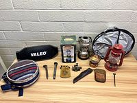 Complete lot of assorted vintage items and lanterns on table against brick wall.