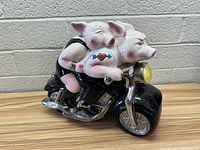 View of two hand painted pigs riding a black motorcycle cookie jar, showing detailed ceramic work and facial expressions