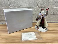 Porcelain Santa figurine with Lenox box and certificate on a light wood surface against a concrete block wall.