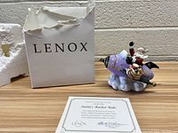 Porcelain figurine of Santa riding a purple and gold rocket on a cloud base, with original Lenox box behind and certificate of authenticity in front.