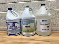 Front view of 3 one-gallon containers of cleaning products including bleach, Liqui Bac, and hand sanitizer.