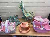 Overview of multiple baby doll carriages, pink baby doll walker, crocheted baby doll blanket, and other doll bedding on a wooden table
