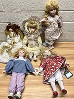 Lot includes five porcelain dolls arranged on a wooden surface against cinder block wall.