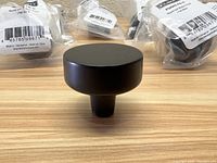 Close-up of one round flat black knob showing its smooth, flat top and cylindrical base on a wooden surface.