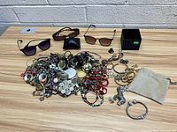Overview of assorted jewelry and three pairs of sunglasses on table