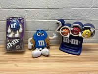 Vintage blue M&M collectible figurine in original packaging alongside a 2000 M&M's promotional display featuring three colorful M&M characters