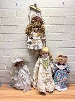 Four dolls displayed together: one hanging doll and three standing dolls on a wooden surface, showcasing styles and outfits.