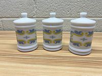 Front view of three milk glass jars with lids showing blue and yellow decorative pattern.