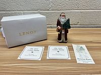 Photo showing the 2001 Lenox Santa figurine, its box, and accompanying documents on a wooden surface