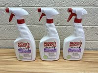 Three bottles of Nature's Miracle Just for Cats Litter Box Odor Destroyer spray arranged side by side on a concrete floor against a concrete wall.