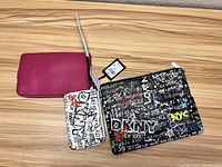 Photo shows three purses: a solid pink purse, a black graffiti-print purse with DKNY branding, and a white graffiti-print smaller purse or wristlet, all new with tags.