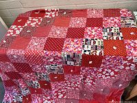 Vintage quilt laid out showing patchwork with floral, striped, polka dots, checkered, and patriotic theme squares in red and white colors.