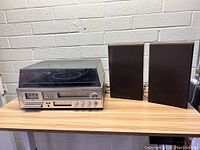 Full view of stereo system with two speakers on either side, on table against brick wall.