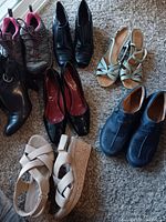 Photo showing all seven pairs of shoes and boots arranged on carpeted floor, including athletic shoes, high heel boots, pumps, wedge heels, sandals, and casual shoes.