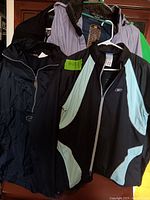 Photo showing multiple jackets including a black hooded coat, a Reebok jacket with light blue sleeves, and a gray/black jacket with Gildan tag.