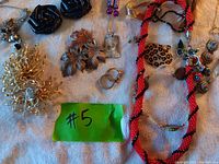 Photo of assorted costume jewelry on fabric surface including beaded necklace, earrings, brooches, and rings.