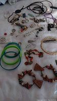 Varied costume jewelry including bracelets in plastic and beaded styles, earrings, and some pins on a white fabric surface.