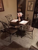 Full view of the round table with four matching metal chairs around it in a carpeted room.