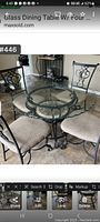 Full view of round glass dining table with scalloped edge and four metal chairs with beige upholstered seats.