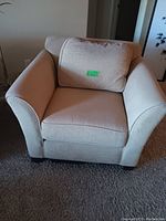 Front view of beige fabric living room chair with loose back cushion and rounded armrests on carpeted floor