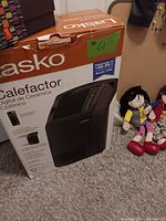 Photo of Lasko ceramic digital cyclonic heater in original box with several Spanish-speaking dolls visible beside it.