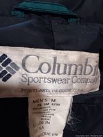 Close-up photo of the label inside a black men's Columbia Sportswear jacket, size medium, showing fabric content and manufacturing details.
