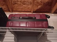 Red hard-shell suitcase with black handle and two wheels shown on shelf.