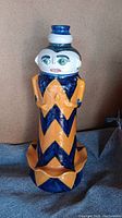 Front and side views of a signed Mexican pottery vase shaped like a figure with blue and yellow zigzag motif and white painted face.