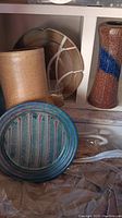 Pottery collection including tan crackled glaze vases, a multicolor round plate, and a pottery tissue holder with a scalloped edge plate visible in back.
