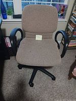Front view of brown fabric office chair with black armrests and five-wheel base, positioned indoors on carpet.
