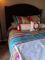 Wooden queen size bed frame with colorful bedding and pillows placed on mattress.