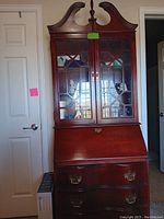 Full front view of wooden secretary desk with glass cabinet doors on upper section and multiple lower drawers.