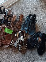 Image showing five different pairs of women's sandals in brown, black, gold, and patterned colors, arranged on carpeted floor.