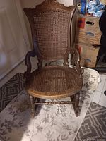 Front view of the small wooden rocking chair showing cane seat and back with carved wood frame and armrests.