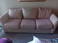 Full frontal view of the sofa showing three seat and back cushions, beige upholstery, on carpeted floor with some staining visible on cushions.