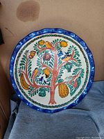 Full front view of the extra large pottery bowl with colorful painted tree, fruits, and birds, showing its circular blue scalloped rim.