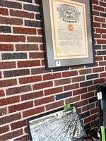 Wide view of two framed pieces leaning against a brick wall. Top piece is the charter document, below is the photograph.