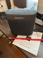 Black Bose SoundLink Color II speaker with Bose logo visible and user manual beneath.