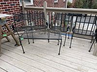 Photo of wrought iron loveseat, two chairs, and coffee table set on outdoor wooden deck, showing condition and design of furniture.