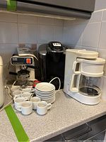 Three coffee makers and espresso cups arranged on kitchen counter