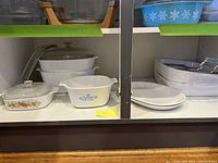 Shelf of CorningWare casseroles and platters in Blue Cornflower, Spice of Life, and plain patterns showing a variety of ceramic dishes with glass lids