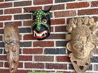 Three carved wooden decorative masks hung on a brick wall, showing the full set and relative sizes.