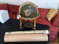 Globe on wooden stand with two rolled maps lying flat and a cardboard tube on a black table.