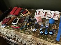 Overall view of lot items on a table, showing key chains, wallets, grooming kits, pocket cutlery, blue glass evil eyes, umbrella, and folders.