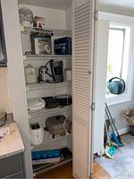 Photo of pantry shelves showing various kitchen appliances including a white toaster, black waffle iron, electric frying pan, and boxes of mixers.