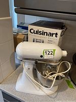KitchenAid Hobart K45SS stand mixer with bowl, white, front-left angle view showing model and brand plaque with Hobart division, on kitchen counter with box labeled Cuisinart Professional Series behind it.