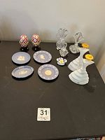 Overall view of entire lot showing eggs, plates, perfume bottles, and figurines on black surface