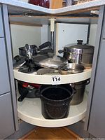 Kitchen corner cabinet with lazy Susan filled with assorted pots, pans, and lids mostly Revere Ware with at least one visible black enamel Le Creuset pan.